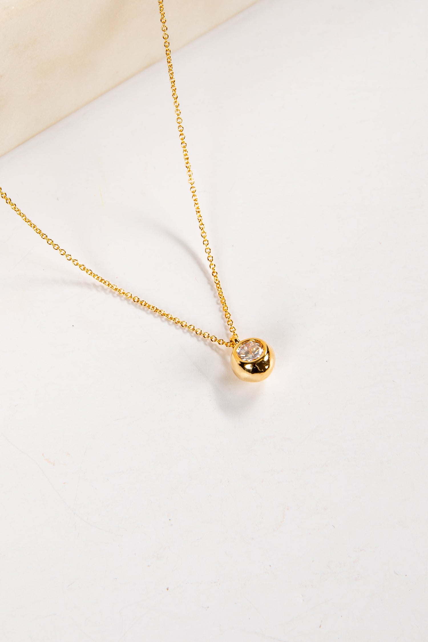 Gold necklace with a small pink gemstone pendant on a white background