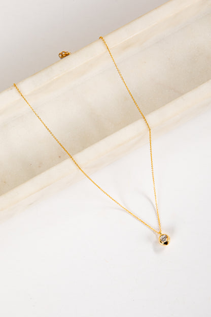 Gold necklace with a small pendant on a white surface