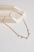 A delicate gold chain necklace with small clear crystal pendants and tiny gold beads, displayed on a white surface next to a cream-colored stone prop.