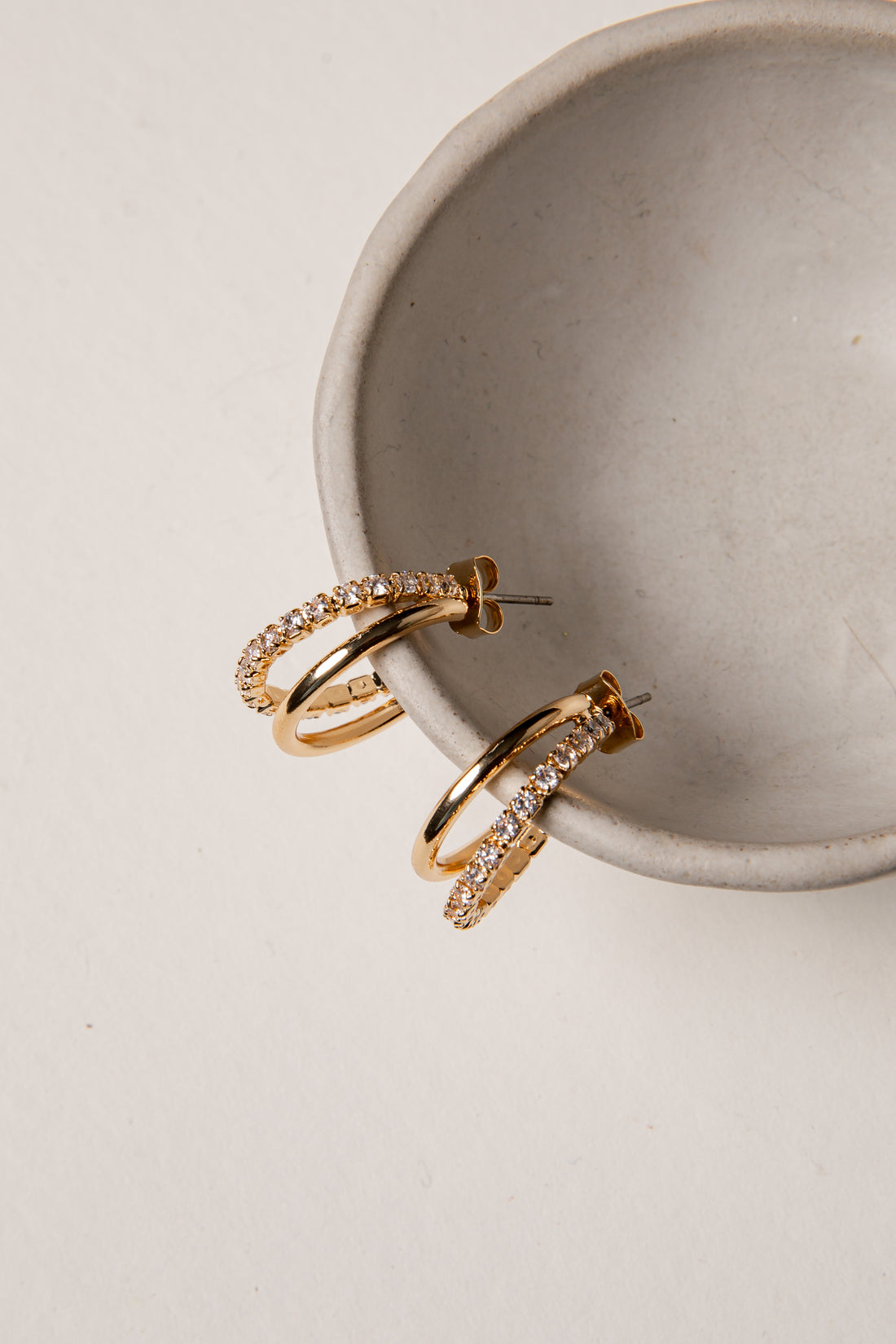 Gold hoop earrings with diamond accents on a beige surface.