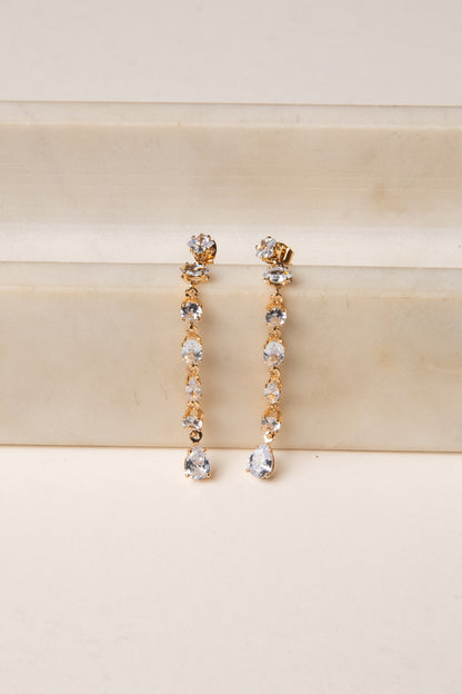 Gold and silver drop earrings on a beige surface