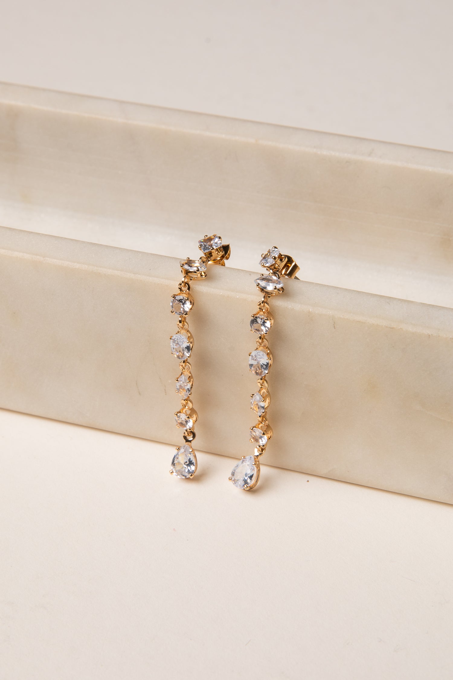 Gold and crystal drop earrings on a beige surface
