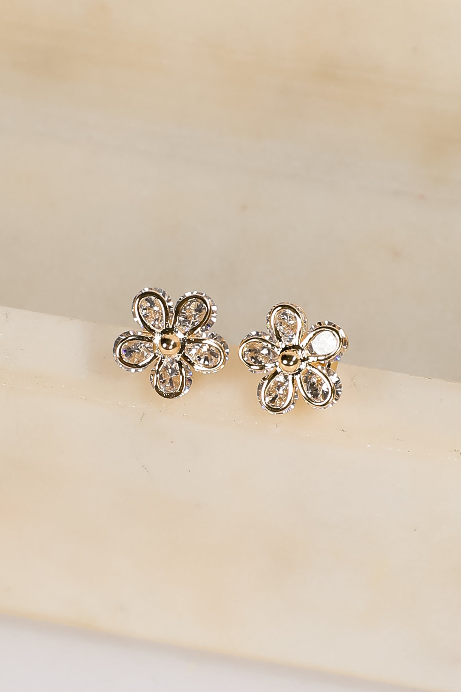 Flower-shaped earrings with clear stones on a beige background