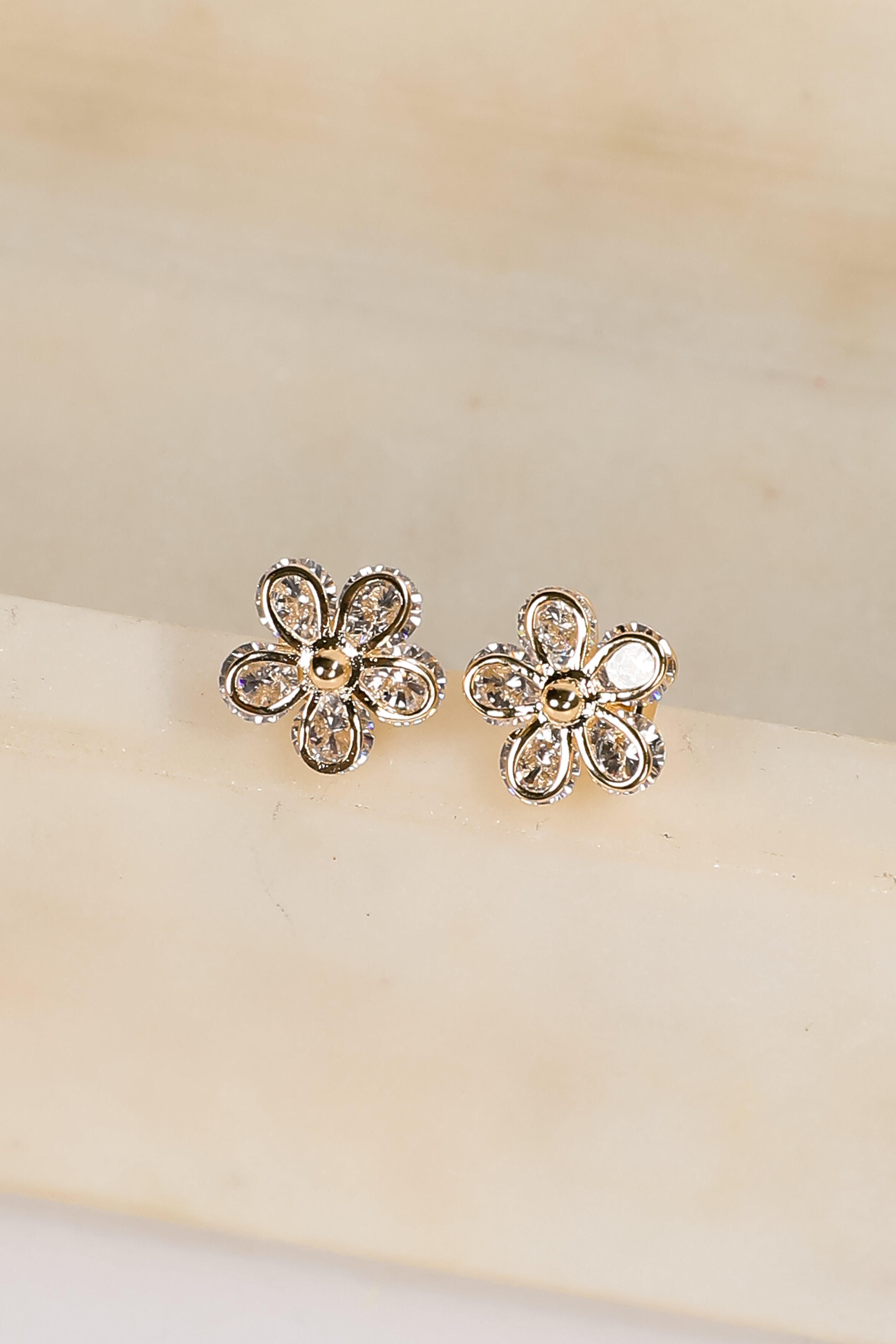 Flower-shaped earrings with clear stones on a beige background