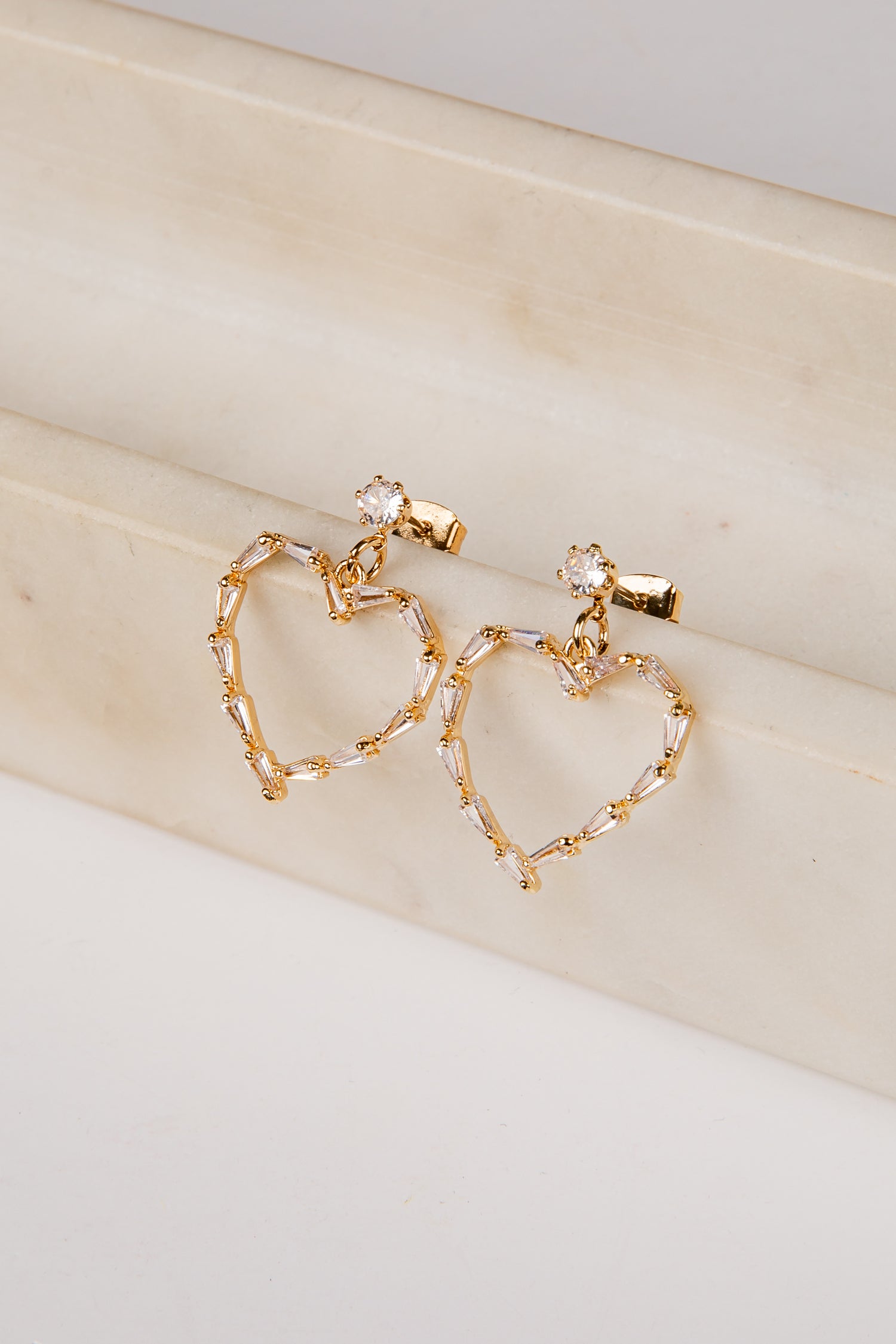 Gold heart-shaped earrings on a beige surface