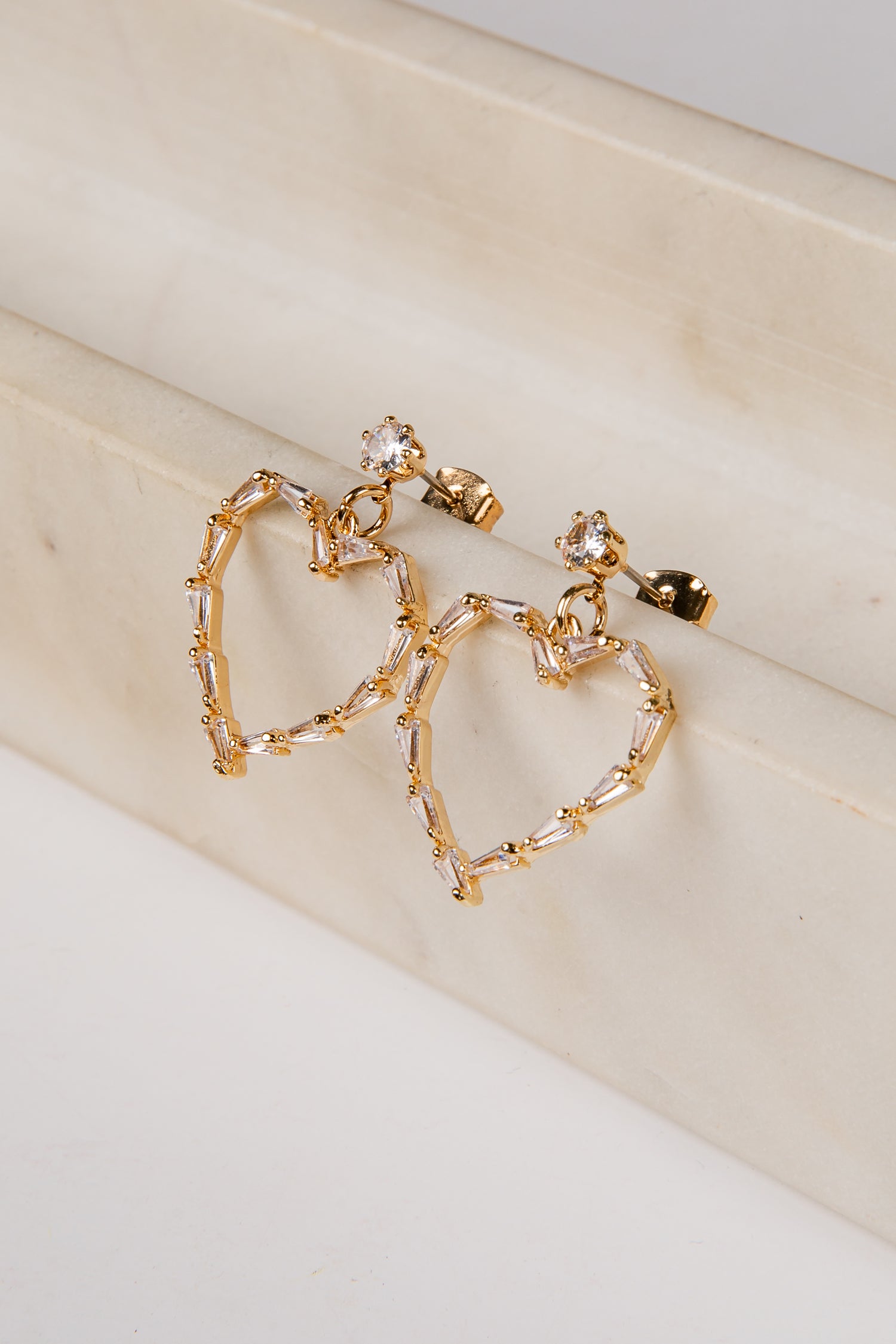 Gold hoop earrings with heart-shaped designs on a beige surface
