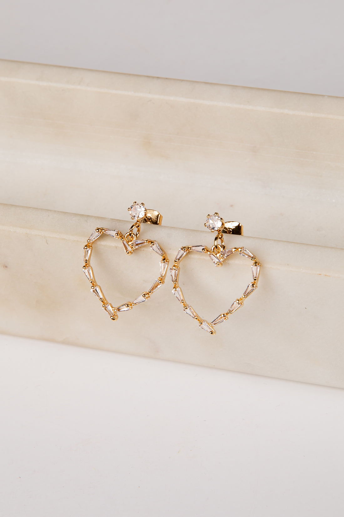 Gold heart-shaped earrings on a light wooden surface