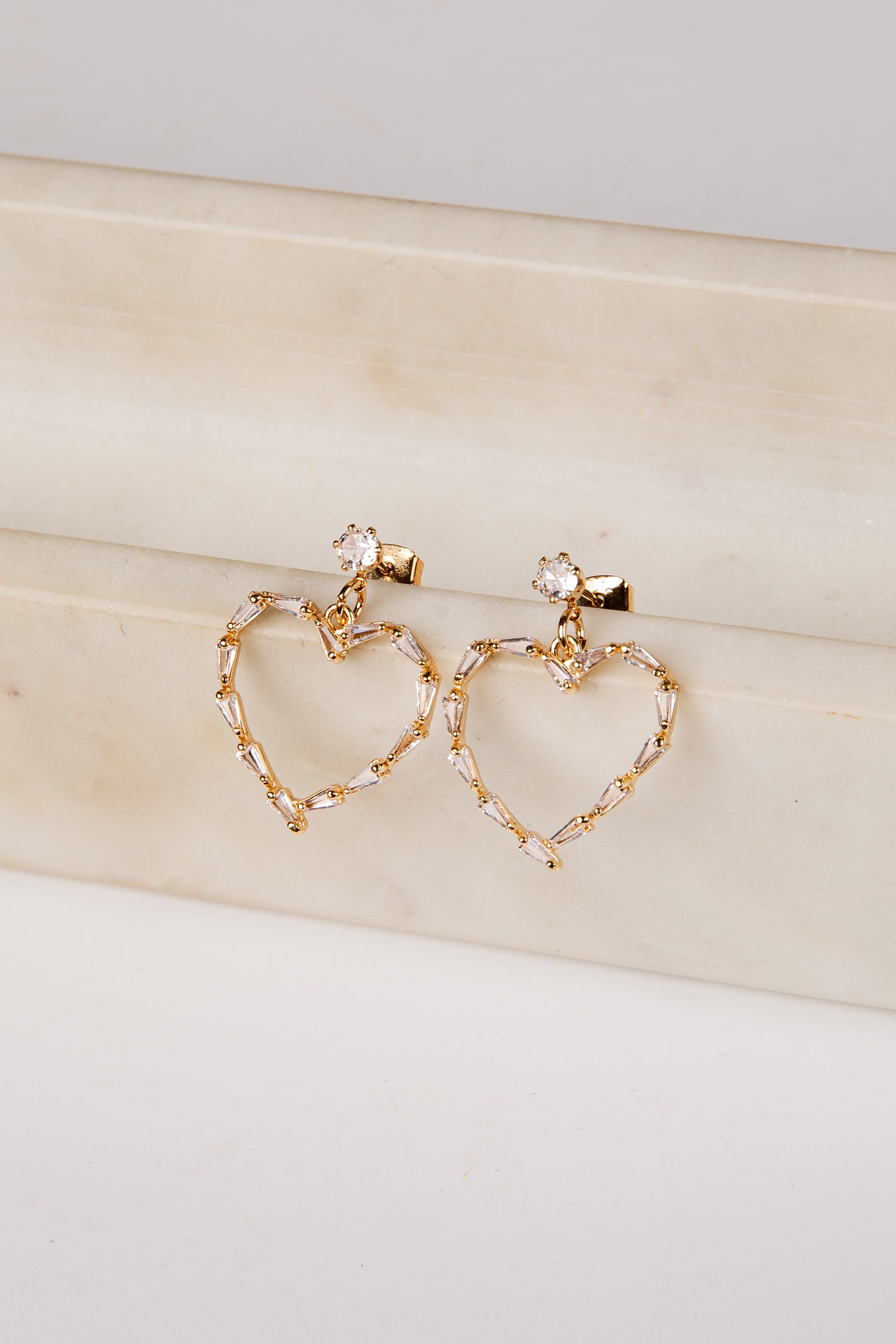 Gold heart-shaped earrings on a light wooden surface