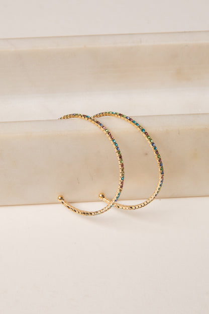 Gold hoop earrings with multicolored beads on a beige surface