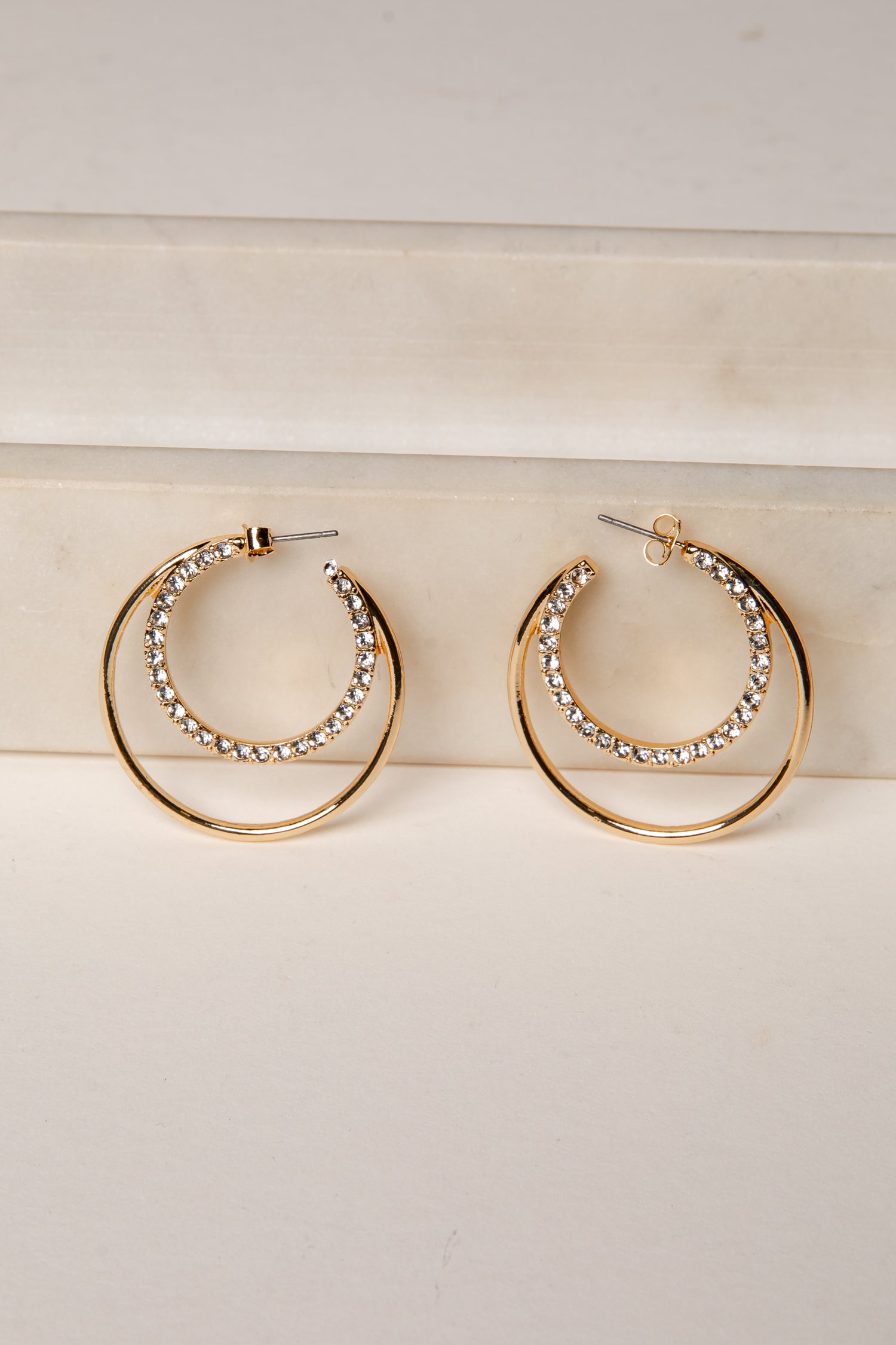 Gold hoop earrings with rhinestone detailing on a light wooden surface.