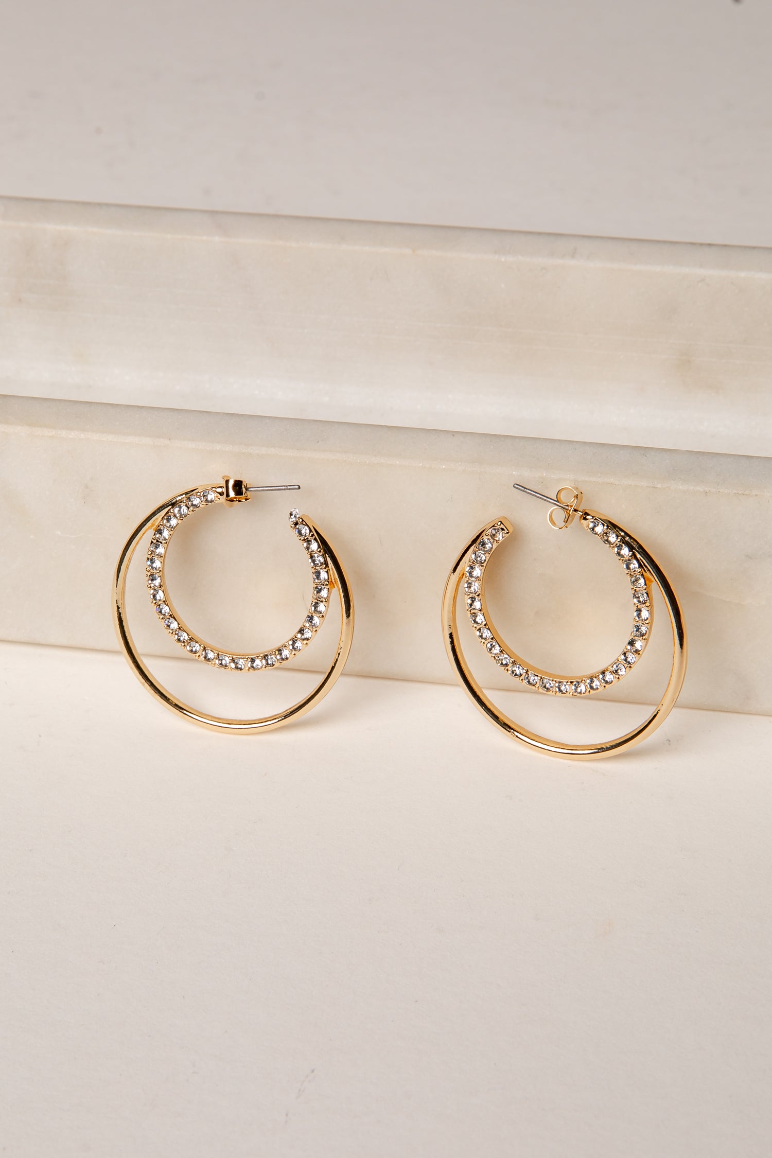 Gold hoop earrings with embedded stones on a light beige surface