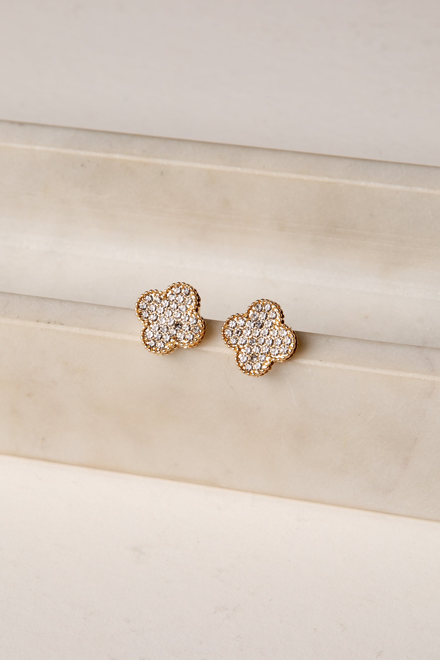 Pair of gold floral earrings with clear gemstones on a beige surface.