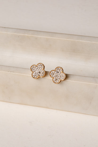 Pair of gold floral earrings with clear gemstones on a beige surface.