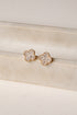 Pair of gold floral earrings with clear gemstones on a beige surface.