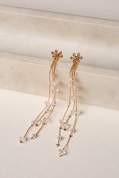 Gold and pearl earrings on a light beige surface