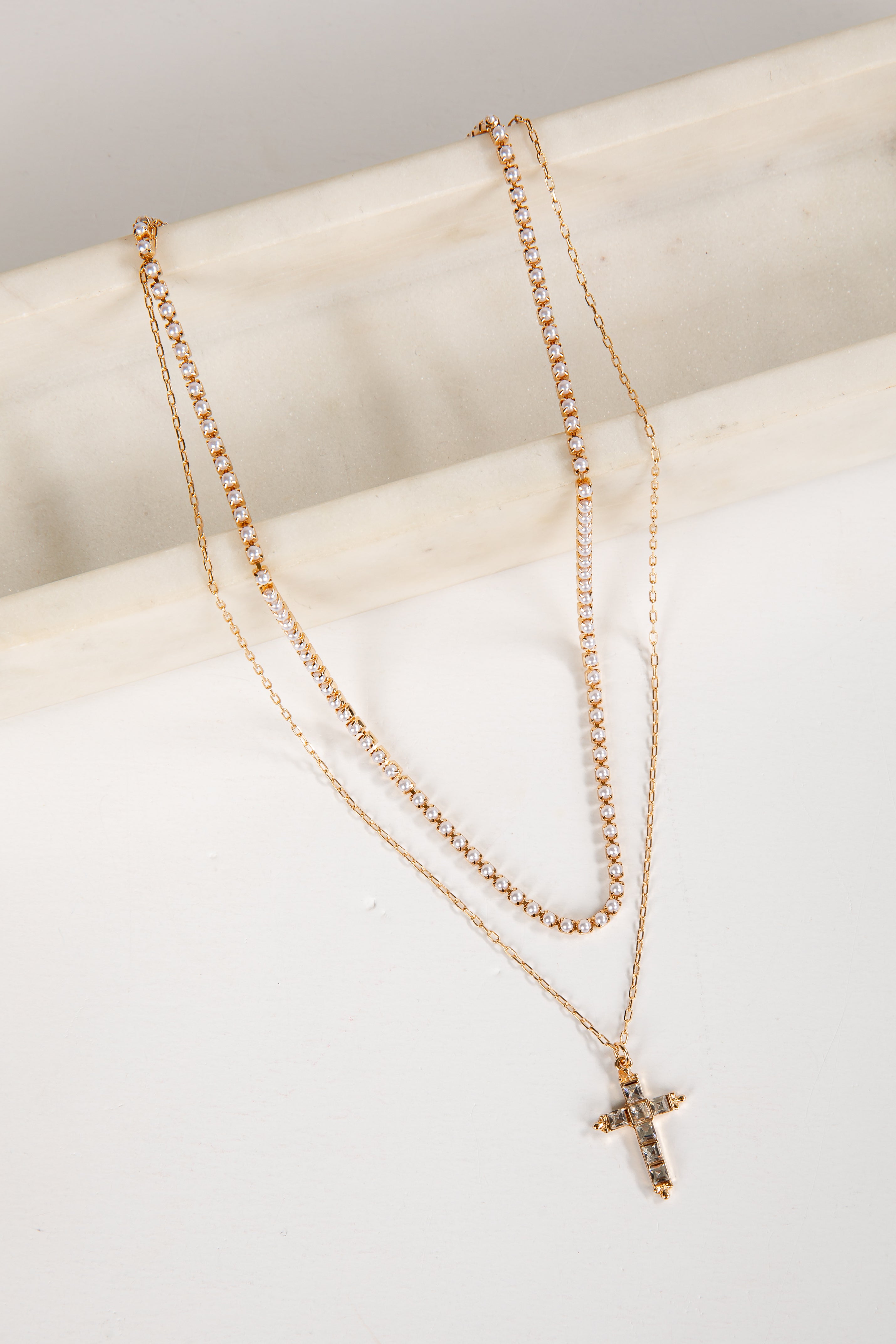 Two gold necklaces with a cross pendant on a white surface