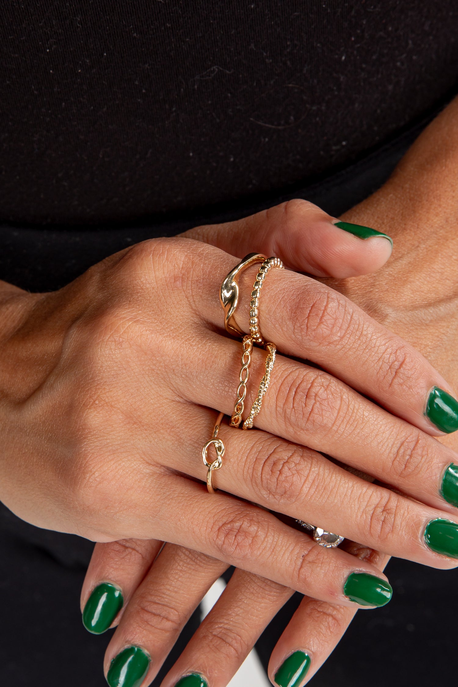 Close-up of a hand wearing gold rings with green nail polish on a black background