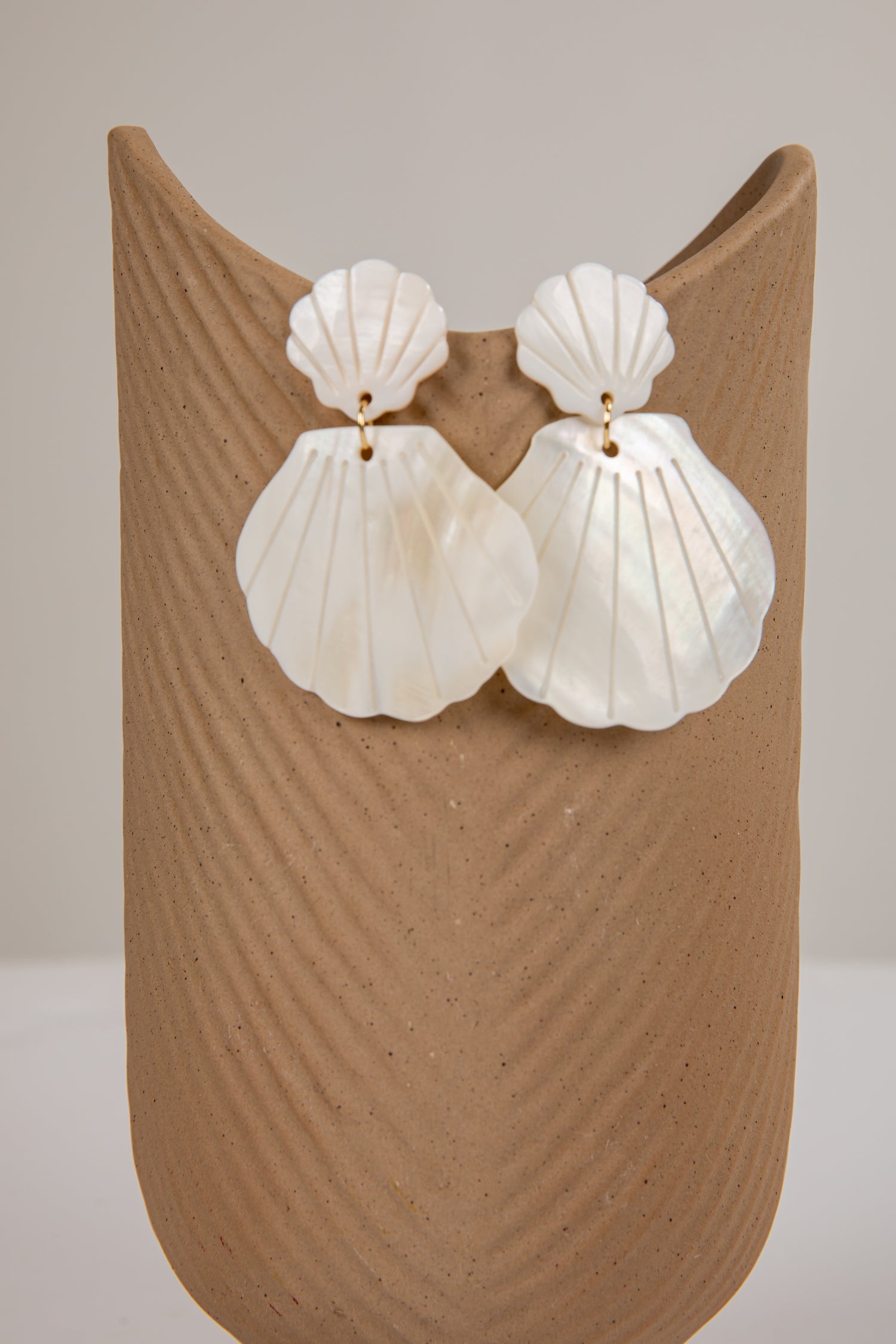 Shell-shaped earrings on a beige stand against a neutral background