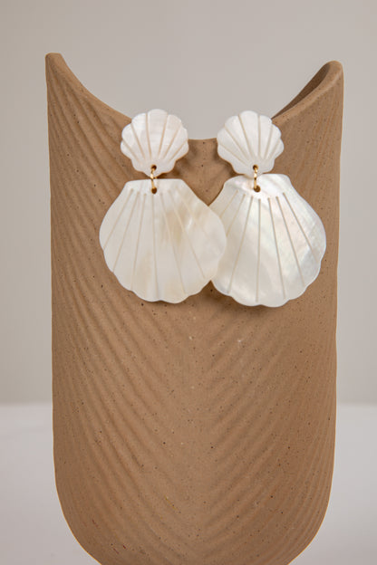 Shell-shaped earrings on a beige stand against a neutral background