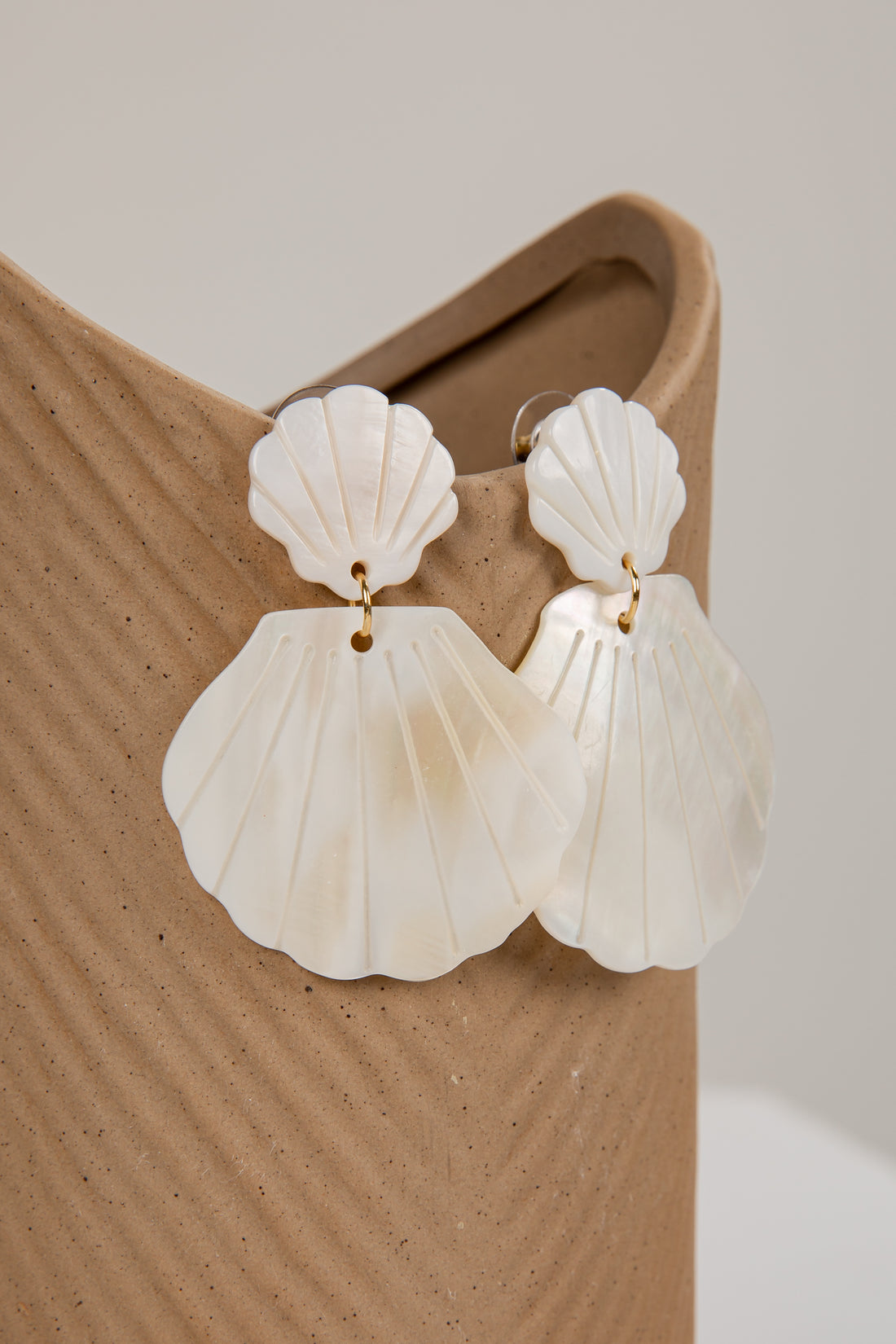 Shell-shaped earrings on a beige stand against a neutral background