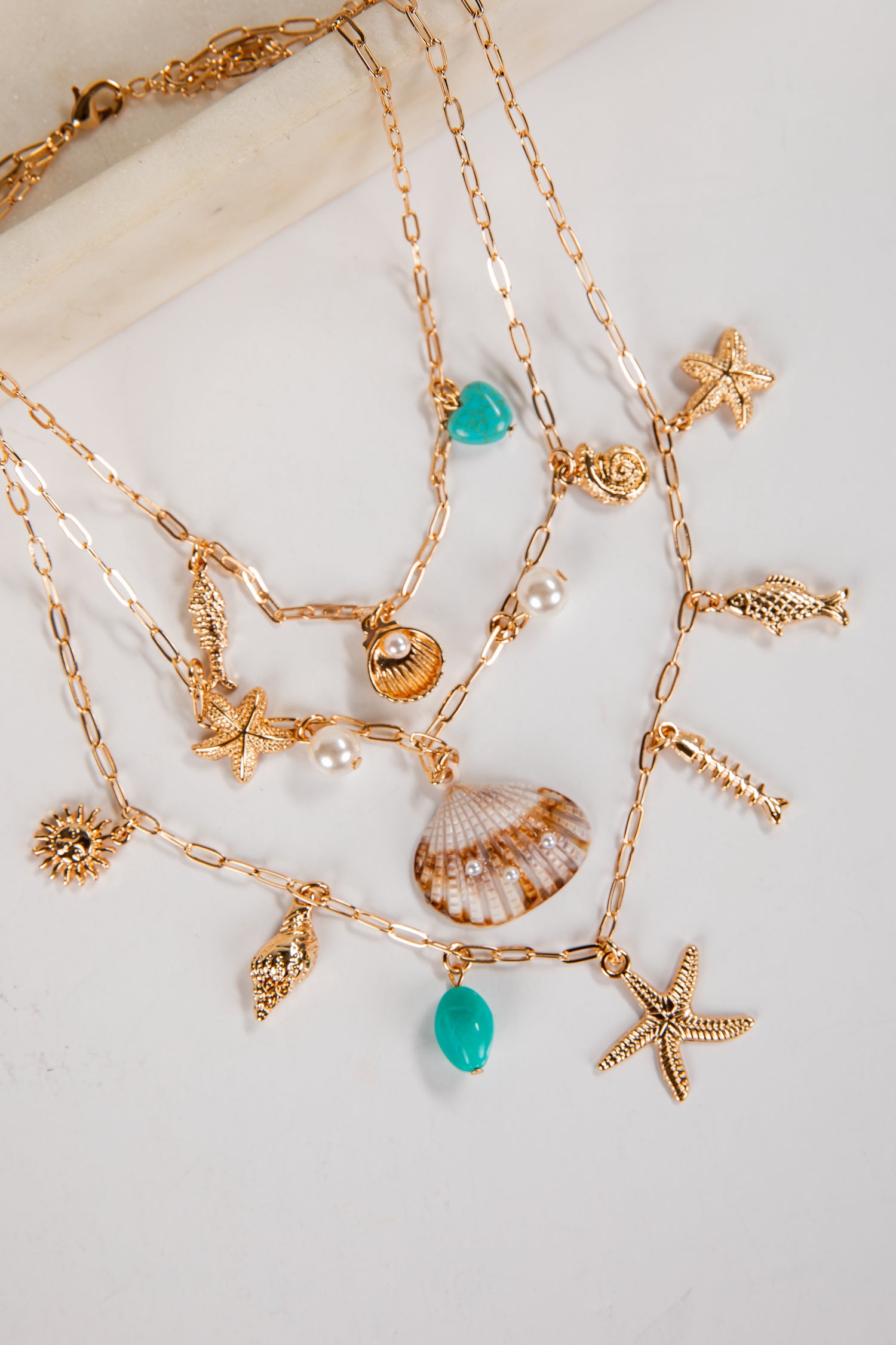Gold necklaces with various charms including stars, shells, and turquoise beads on a light background.