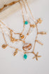 Gold necklaces with various charms including stars, shells, and turquoise beads on a light background.
