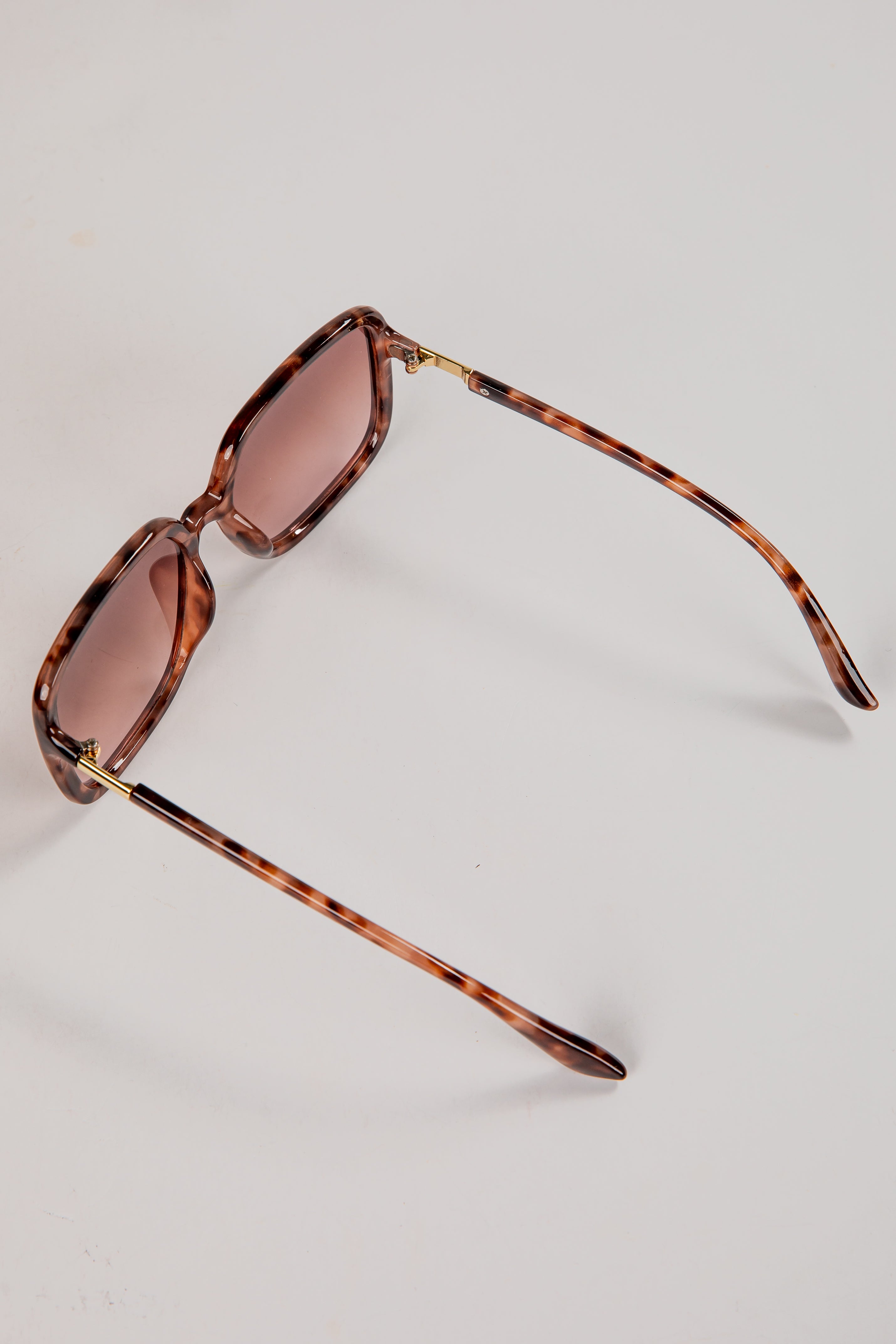 Sunglasses with tortoiseshell frame and brown lenses on a light gray background