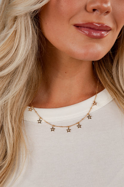Close-up of a woman wearing a gold star necklace against a neutral background