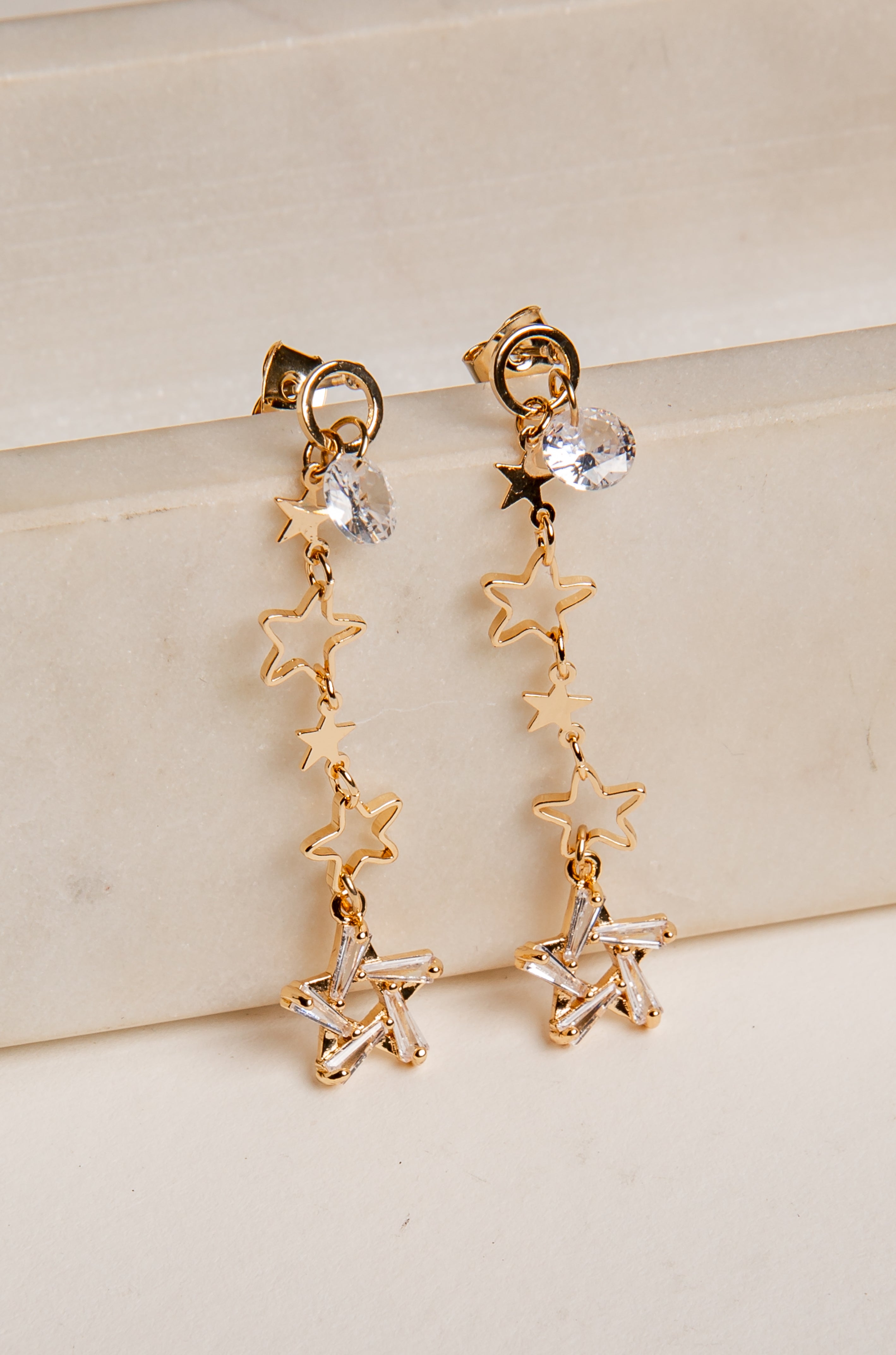 Gold star-shaped earrings with clear stones on a beige surface