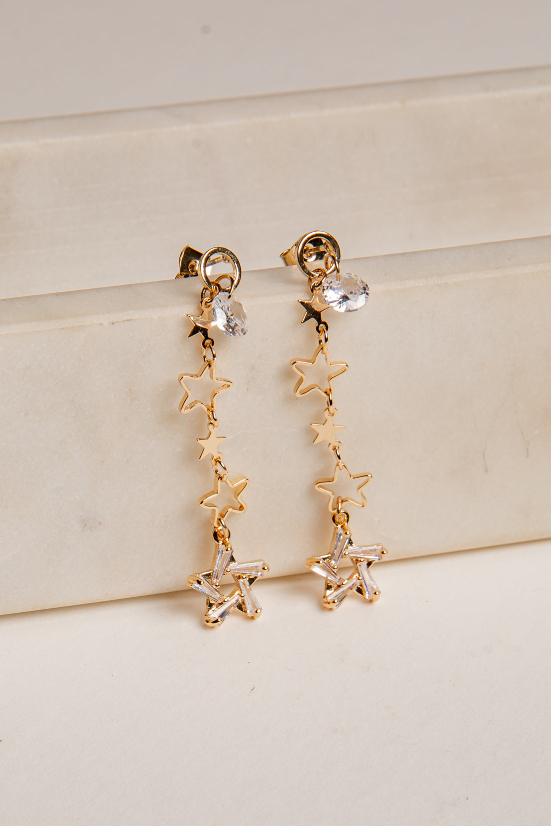 Gold star-shaped earrings on a light beige surface