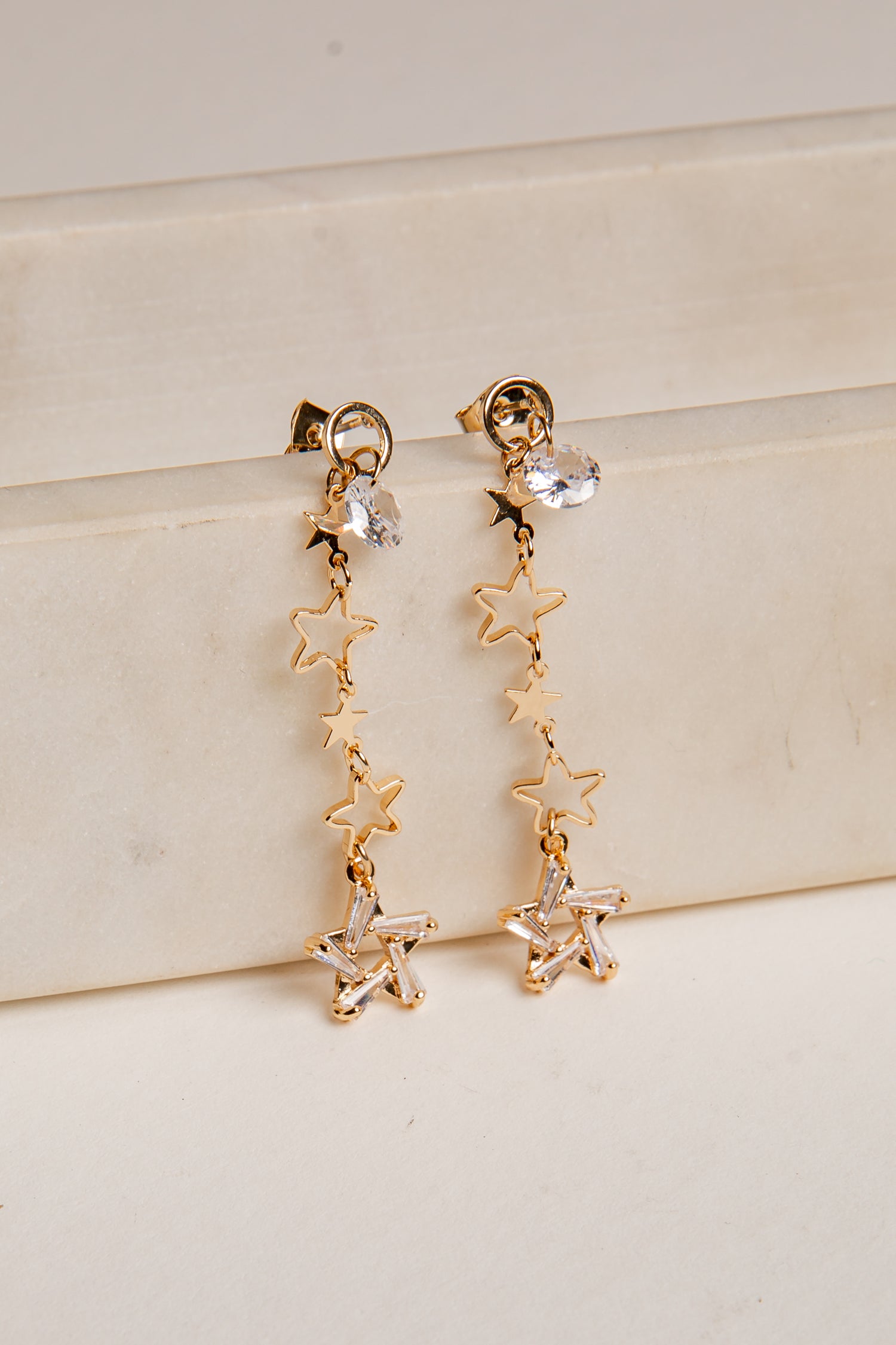 Gold star-shaped earrings on a light beige surface