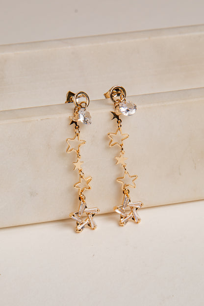Gold star-shaped earrings on a light beige surface
