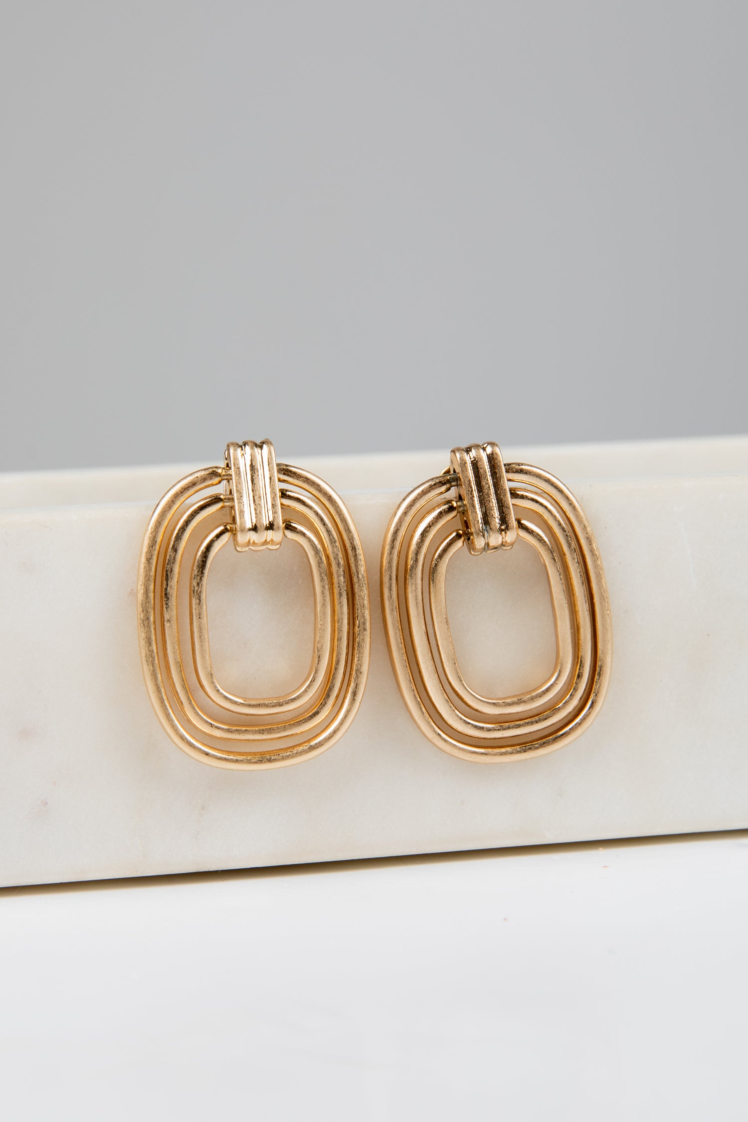 Gold hoop earrings on a white surface with a gray background