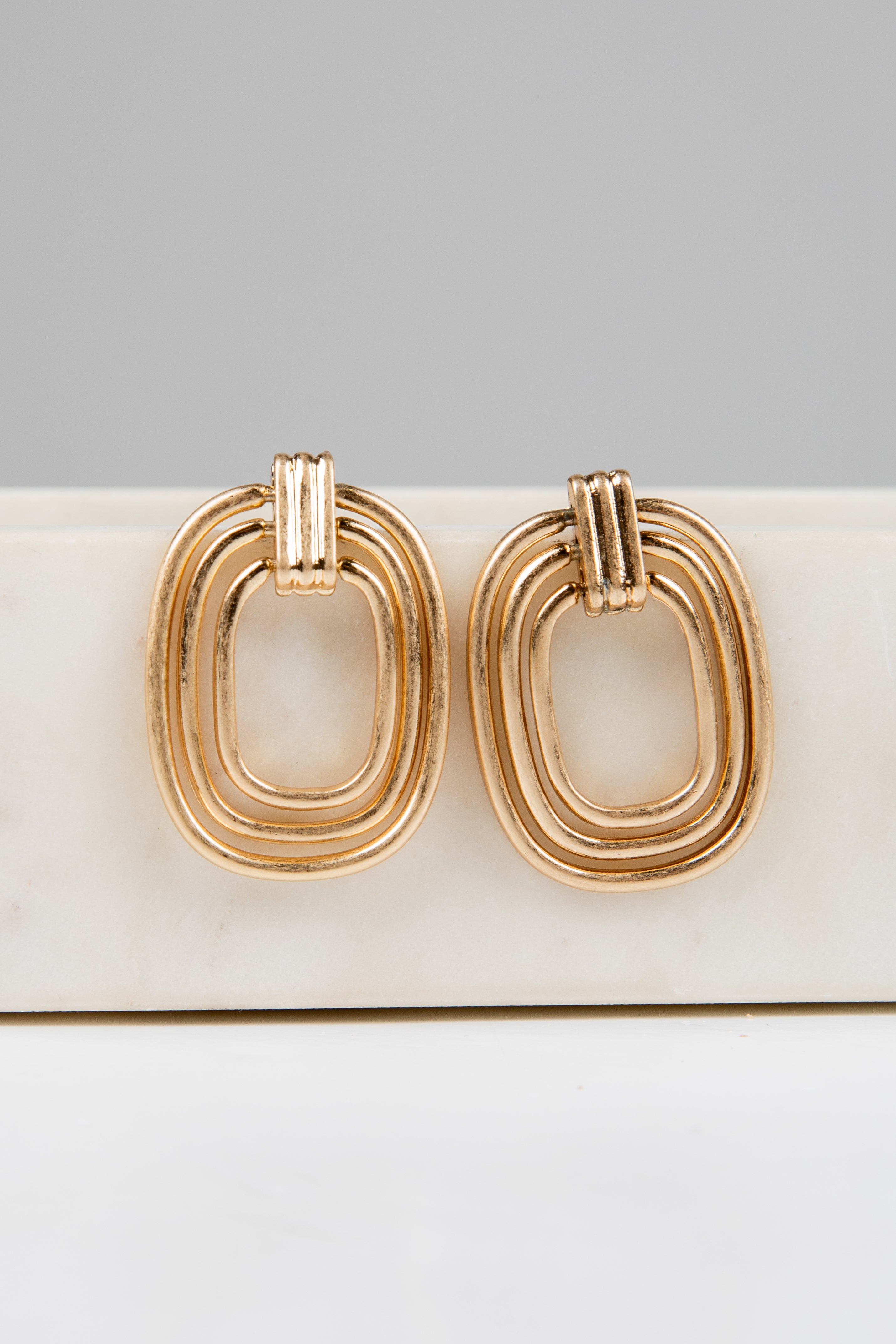 Gold hoop earrings on a white surface with a gray background