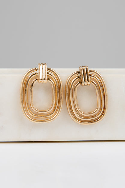 Gold hoop earrings on a white surface with a gray background