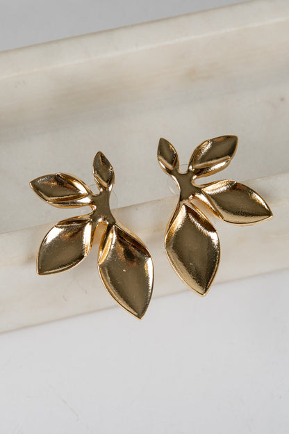 Gold leaf-shaped earrings on a light background