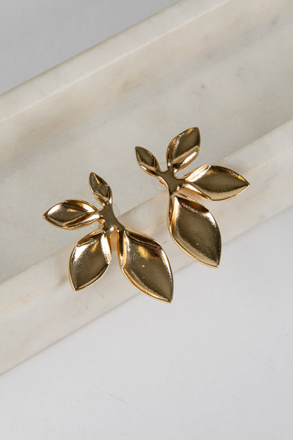 Gold leaf-shaped earrings on a marble surface