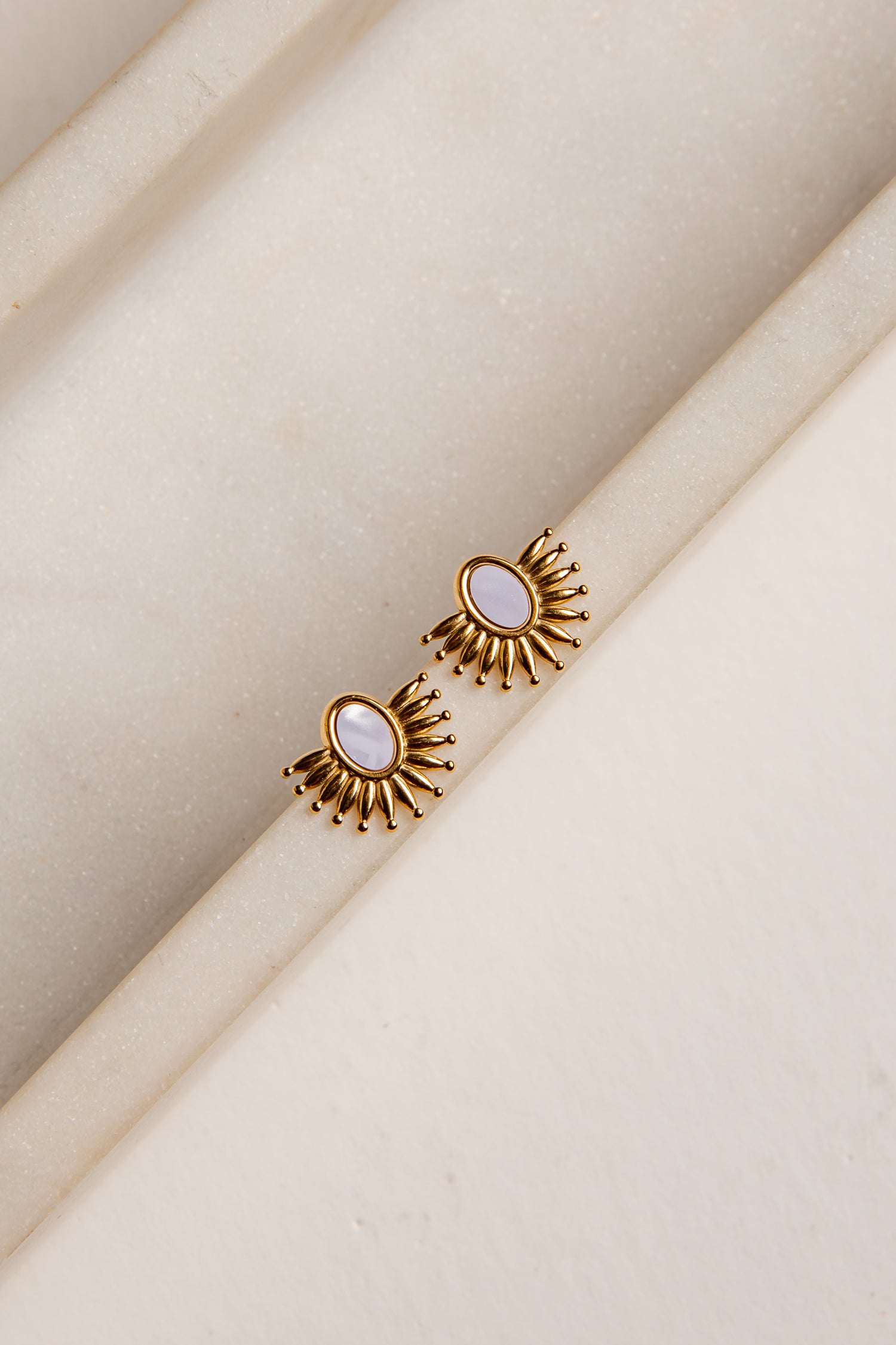 Gold earrings with a central gemstone on a beige fabric background