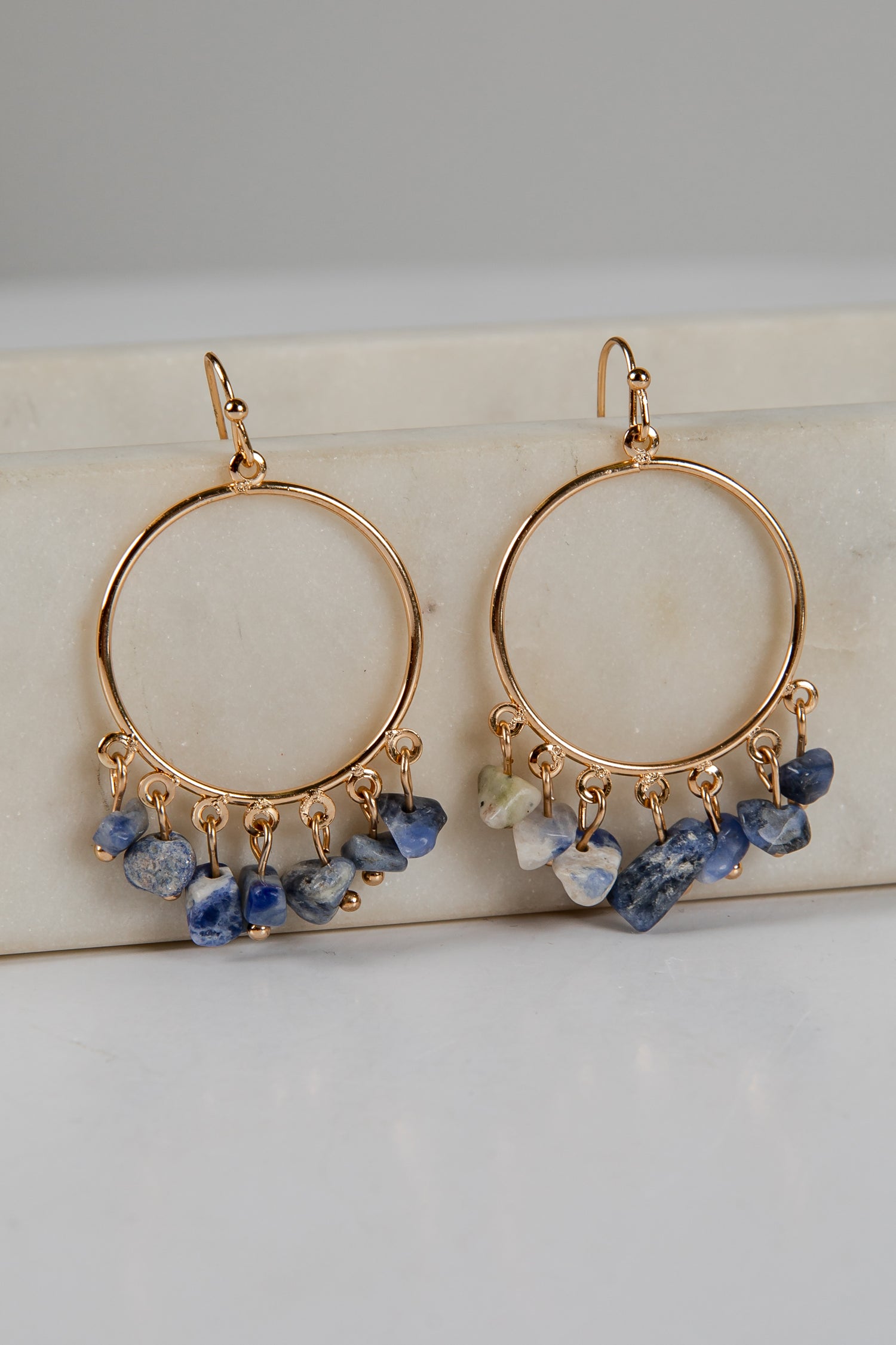 Gold hoop earrings with blue and green gemstone drops on a light background