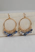 Gold hoop earrings with blue and green gemstone drops on a light background