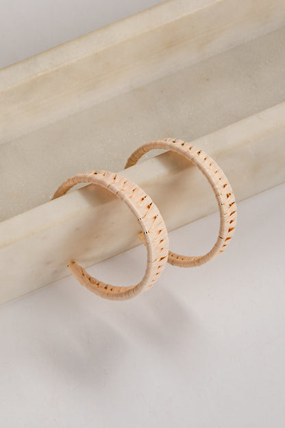 Two gold hoop earrings on a light wooden stick against a neutral background