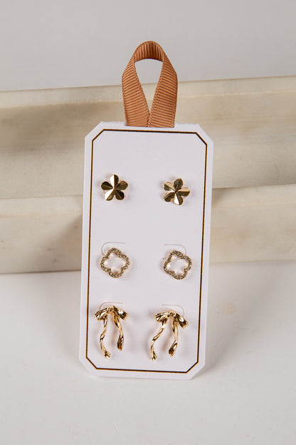 Set of gold earrings on a white card with a brown ribbon, against a neutral background.