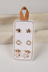 Set of gold earrings on a white card with a brown ribbon, against a neutral background.