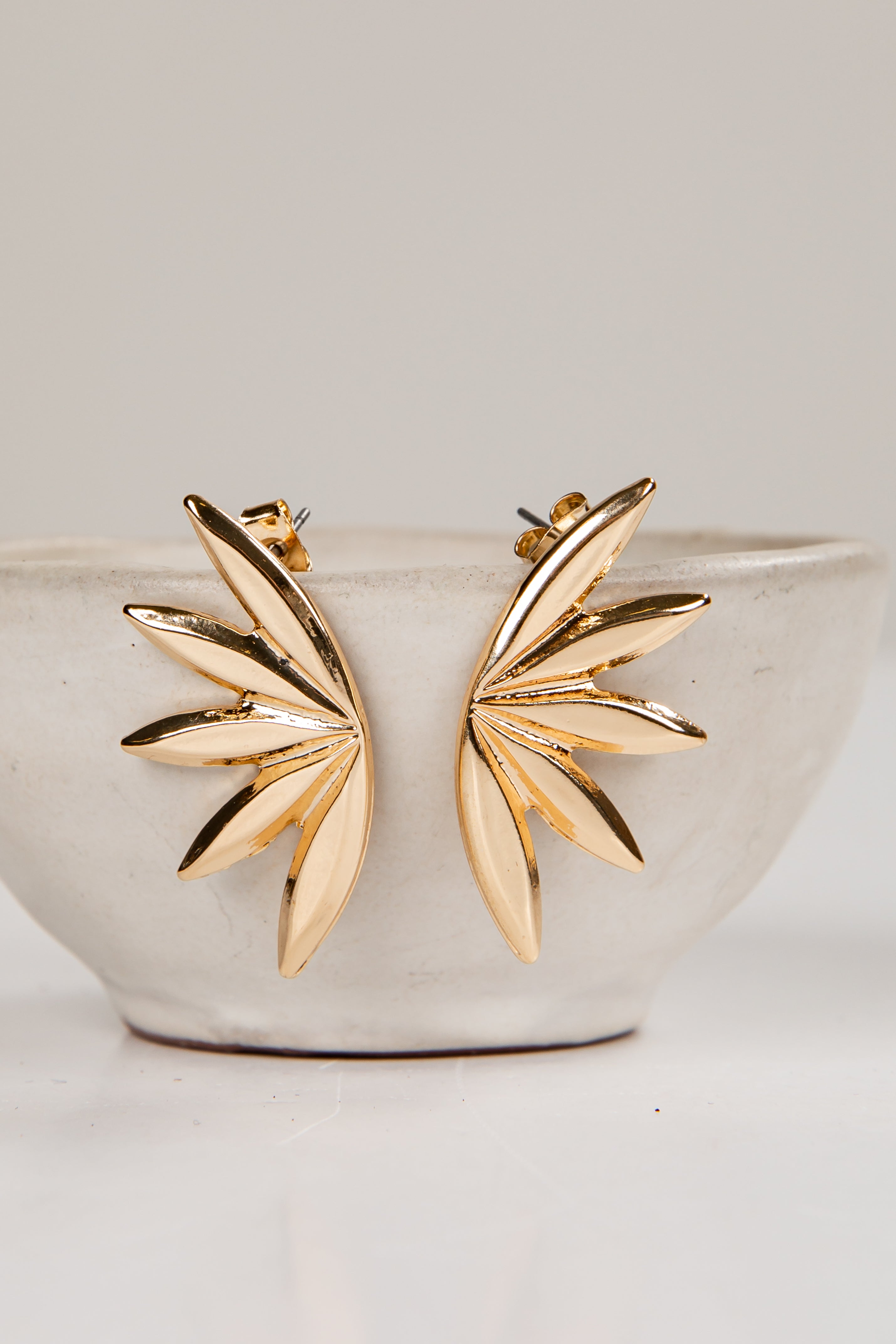 Gold leaf-shaped earrings on a white ceramic bowl with a light gray background
