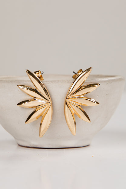 Gold leaf-shaped earrings on a white ceramic bowl with a light gray background