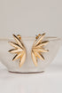 Gold leaf-shaped earrings on a white ceramic bowl with a light gray background
