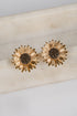 Gold sunflower-shaped earrings on a light beige surface