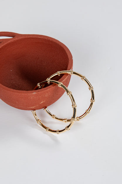 Gold hoop earrings on a white surface with a terracotta dish.