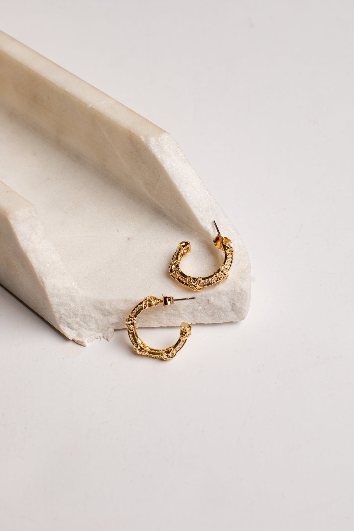 A pair of textured gold hoop earrings resting on a white stone tray against a clean white background.