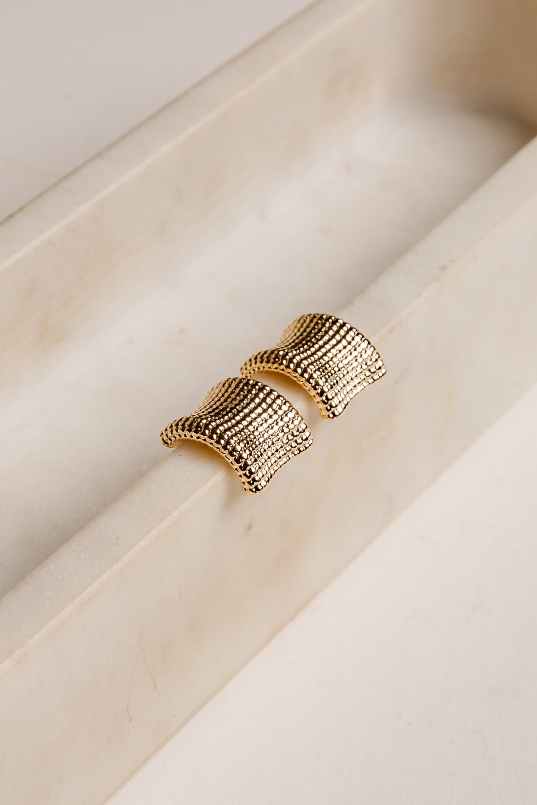 Gold textured earrings on a light wooden surface